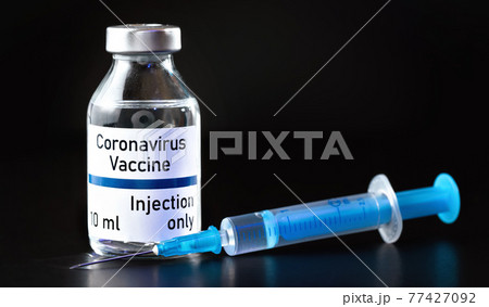 Coronavirus Covid 19 vaccine concept (own design, not real product) - small glass bottle with silver cap, syringe near, closeup detail on black background Coronavirus Covid 19 vaccine concept (own design, not real product) - small glass bottle with silver cap, syringe near, closeup detail on black background 77427092