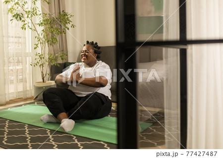 Woman wearing sport clothes soothing her breath while doing breathing exercises 77427487