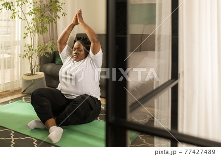 Woman holding her hands above her head and sitting in lotus posture Woman holding her hands above her head and sitting in lotus posture 77427489