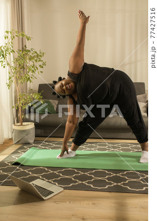 Woman repeating exercises while watching online workout session at home 77427516