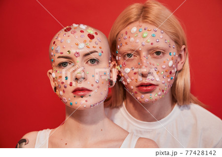 Albino feminine man and bald masculine woman with decor at their faces looking at the camera 77428142