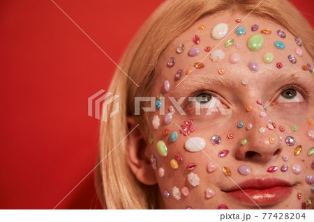 Blonde long haired man looking away while posing with rhinestones at his face Blonde long haired man looking away while posing with rhinestones at his face 77428204