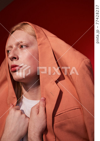 Albino male with womanlike appearance wearing orange jacket at his head 77428237