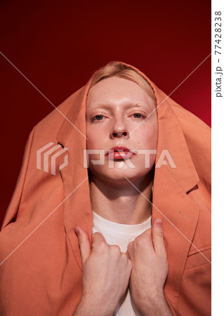 Man with feminine appearance looking at the camera while wearing stylish jacket at his head 77428238