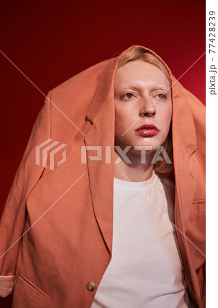 Man with feminine appearance wearing stylish jacket at his head posing at the studio 77428239