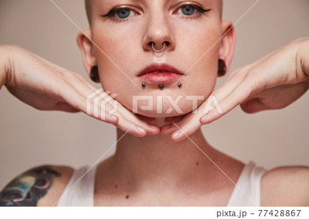 Woman with piercing at her face and ear tunnels posing with hands near her face 77428867