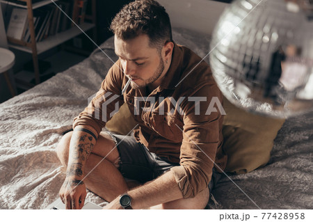 Man smoking hand rolled cannabis cigarette and working at the laptop 77428958
