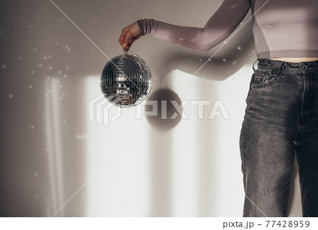 Unrecognizable woman holding disco ball in front of the white wall Unrecognizable woman holding disco ball in front of the white wall 77428959