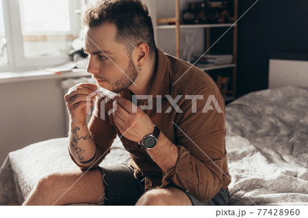 Man sitting at table and rolling with his tongue hand rolled cannabis cigarette 77428960