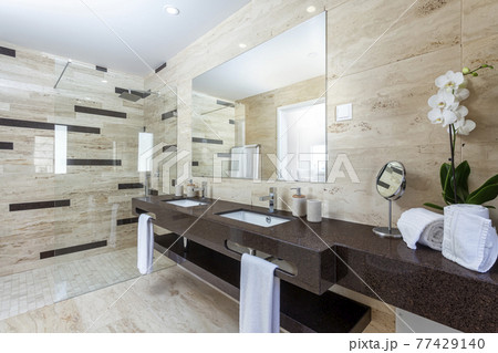 Modern tiled gray bathroom of a resort, with a sink facing a toilet and a shower at the end of the room. Modern tiled gray bathroom of a resort, with a sink facing a toilet and a shower at the end of the room. 77429140