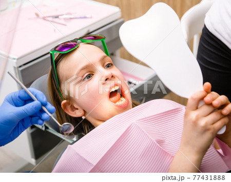Preteen girl looking at her cured teeth in the mirror in pediatric dental clinic Preteen girl looking at her cured teeth in the mirror in pediatric dental clinic 77431888