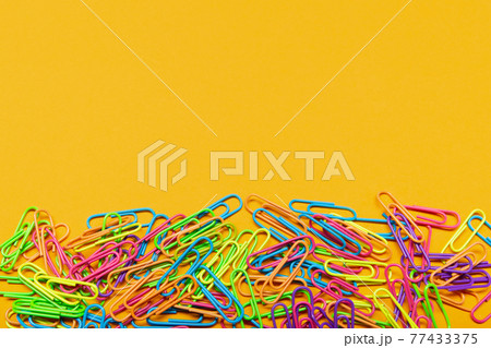 multicolored paper clips lie on a yellow background, with copy space, a bunch of paper clips 77433375