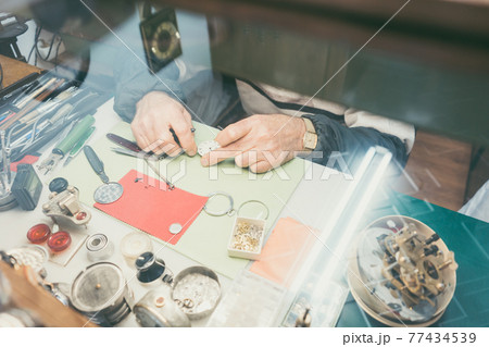 Top-down view on hands of watchmaker sitting at his workbench Top-down view on hands of watchmaker sitting at his workbench 77434539