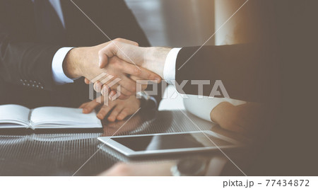 Unknown businessmen shaking hands above the glass desk in a modern office, close-up. Unknown business people at meeting. Teamwork, partnership and handshake concept Unknown businessmen shaking hands above the glass desk in a modern office, close-up. Unknown business people at meeting. Teamwork, partnership and handshake concept 77434872