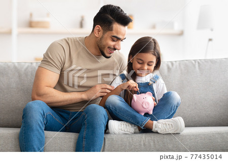 Little girl and dad saving money in piggy bank Little girl and dad saving money in piggy bank 77435014