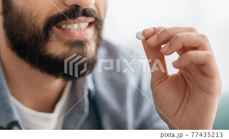 Medication treatment concept. Unrecognizable bearded smiling man taking pill, cropped, closeup Medication treatment concept. Unrecognizable bearded smiling man taking pill, cropped, closeup 77435213