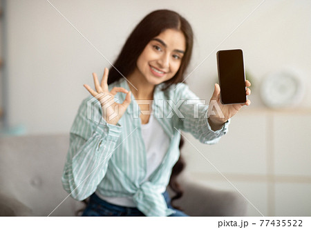 Charming Indian woman showing cellphone with empty screen, gesturing OK at home, mockup for website design Charming Indian woman showing cellphone with empty screen, gesturing OK at home, mockup for website design 77435522