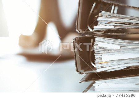 Binders with papers are waiting to be processed by business woman or bookkeeper working at the desk in office back in blur. Audit and tax concept Binders with papers are waiting to be processed by business woman or bookkeeper working at the desk in office back in blur. Audit and tax concept 77435596