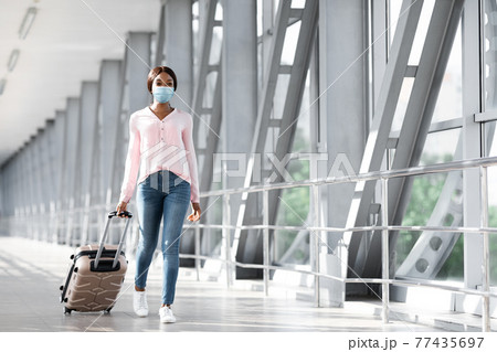 Pandemic Tourism. Young African Female In Medical Mask Walking In Airport Terminal Pandemic Tourism. Young African Female In Medical Mask Walking In Airport Terminal 77435697