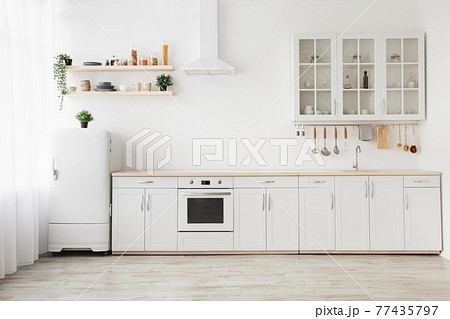 Minimal light scandinavian kitchen interior. White furniture with utensils, shelves with crockery, small refrigerator 77435797