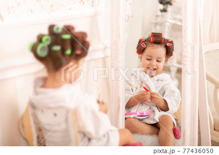 Adorable little girl with curlers paints her fingernails. Copies mom's behavior. Young fashionista. Beauty day Adorable little girl with curlers paints her fingernails. Copies mom's behavior. Young fashionista. Beauty day 77436050