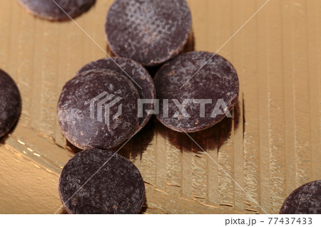 Round chocolate chips on a golden surface. Round chocolate chips on a golden surface. 77437433