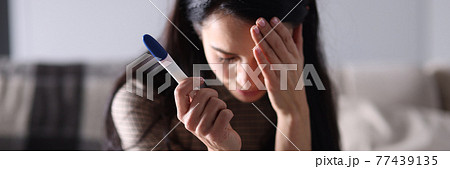 Sad woman sitting on couch and holding pregnancy test closeup 77439135