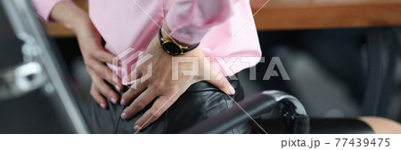 Woman siting on chair in office and holding her lower back closeup Woman siting on chair in office and holding her lower back closeup 77439475