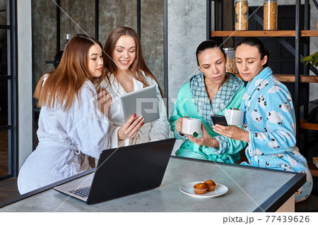 Watching news and messages on mobile devices at breakfast, group of women sits at table in dining room. 77439626