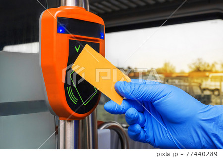 A man's hand in a protective medical glove applies a card to an automatic toll terminal in a modern electric train, close-up A man's hand in a protective medical glove applies a card to an automatic toll terminal in a modern electric train, close-up 77440289