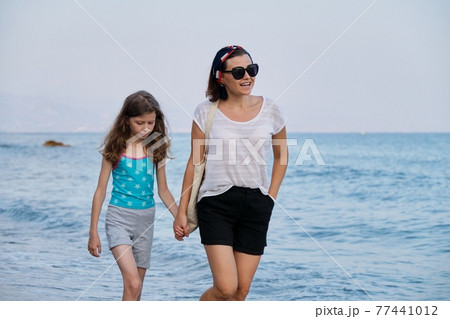 Happy mom and daughter kid walking together on the beach holding hands 77441012