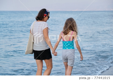 Happy mom and daughter kid walking together on the beach holding hands 77441015