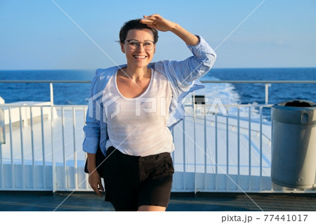 Female in blue shirt on the deck of ship looking at seascape, sky sea sunset background 77441017