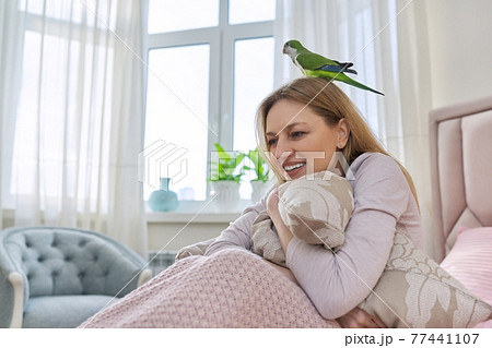 Happy laughing mature woman and green parrot at home in bed Happy laughing mature woman and green parrot at home in bed 77441107