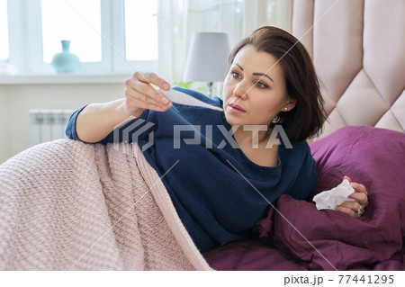Mature sick upset woman with handkerchief looking at thermometer Mature sick upset woman with handkerchief looking at thermometer 77441295