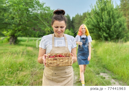 Mother and daughter teenager walking together with basket of fresh strawberries Mother and daughter teenager walking together with basket of fresh strawberries 77441963