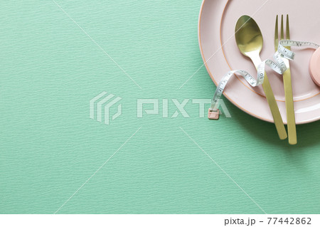 Plate and fork, spoon with measuring tape on green background. Diet concept Plate and fork, spoon with measuring tape on green background. Diet concept 77442862