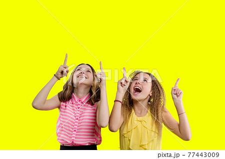 Two emotional teenage girls showing and looking up, copy space yellow background 77443009