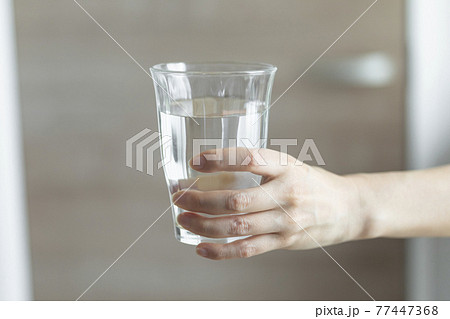 グラスに注いだ水を手に持っているところのイメージ 77447368