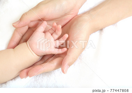 Mother's hand gently wrapping baby's hand on white 77447808