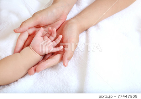 Mother's hand gently wrapping baby's hand on white Mother's hand gently wrapping baby's hand on white 77447809