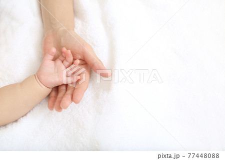 Baby little hand on mom's hand against white sheet 77448088