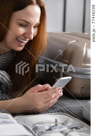 Woman chatting surfing internet use smartphone application during packing suitcase baggage 77448299