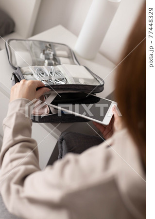 Female hands putting tablet pc into comfortable bag storage get ready to business trip or vacation Female hands putting tablet pc into comfortable bag storage get ready to business trip or vacation 77448329