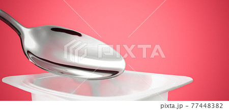 Yogurt cup and silver spoon on red background, white plastic container with yoghurt cream, fresh dairy product for healthy diet and nutrition balance 77448382