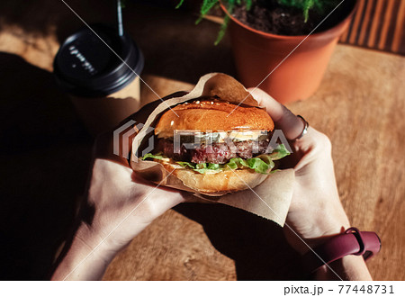 Burger in paper packaging, coffee and fries close-up. Food in a fast food restaurant. Macro photo of a burger with meat and vegetables, French fries and coffee. Fast food set 77448731