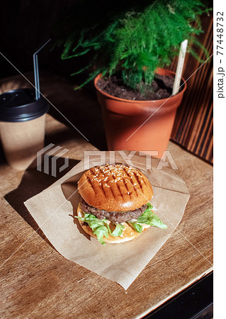 Burger in paper packaging, coffee and fries close-up. Food in a fast food restaurant. Macro photo of a burger with meat and vegetables, French fries and coffee. Fast food set 77448732