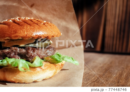 Burger in paper packaging close-up. Food in a fast food restaurant. Macro photo of burger ingredients with meat and vegetables Burger in paper packaging close-up. Food in a fast food restaurant. Macro photo of burger ingredients with meat and vegetables 77448746
