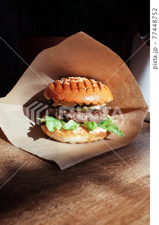 Burger in paper packaging close-up. Food in a fast food restaurant. Macro photo of burger ingredients with meat and vegetables 77448752