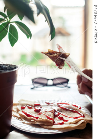 Pancakes drizzled with red syrup on a plate in a restaurant. Breakfast at the cafe. A woman eats pancakes for breakfast from disposable dishes. Top view and vertical photo 77448753